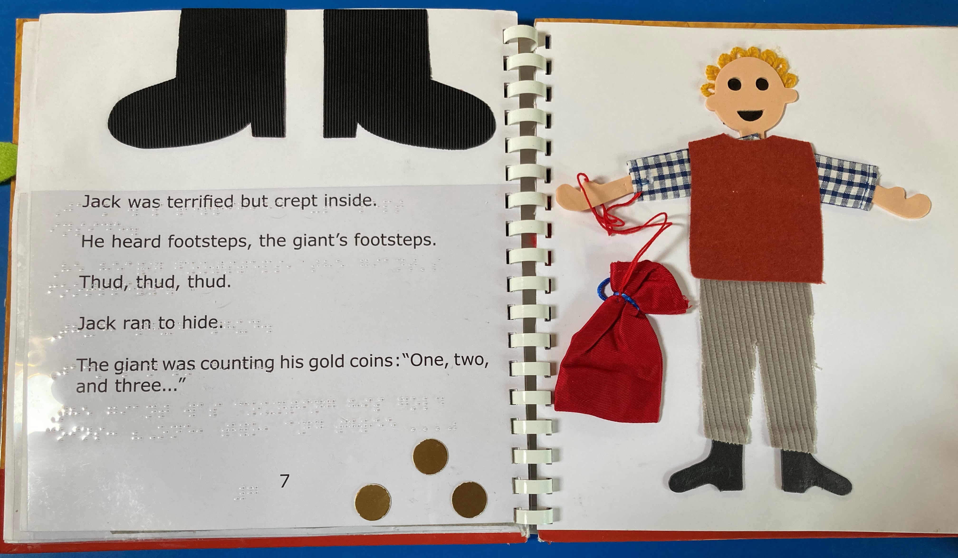 An image from a tactile book of Jack and the Beanstalk. On the right hand page is a picture of Jackholfing a bag of gold coins, on the left hand page is the text in print and braille, some gold coins and large black giant's boots.
